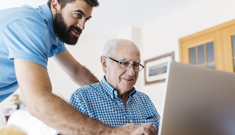 Adult grandson teaching his grandfather to use laptop